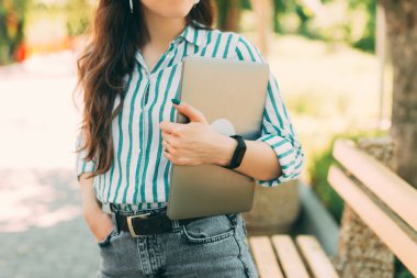 Şehir parkında dizüstü bilgisayar tutan sıradan bir genç kadının kesilmiş fotoğrafı..