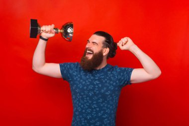 Elinde kupa tutan mutlu sakallı bir adamın portresi ve zaferi kutlamak, kırmızı arka planda durmak.