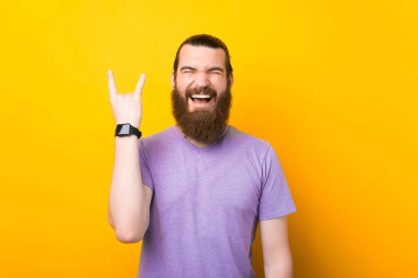 Tişörtlü heyecanlı adam rock 'n roll jestini parmaklarıyla gösteriyor sanki en sevdiği müziği dinliyormuş gibi.