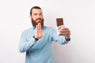 Fotoğrafta sakallı genç adam çikolataya hayır diyor. Elinde çikolatayla el kol hareketi yapıyor.