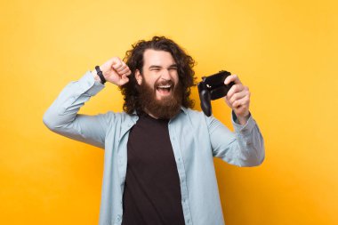 Sarı duvarda çığlık atan sakallı genç bir adamın resmi. Cep telefonuyla oyunlar oynuyor. Kazanan hareketi yapıyor.