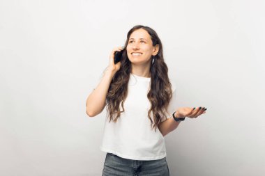 Gülümseyen, sıradan esmer bir kadının portresi beyaz arka planda cep telefonuyla konuşuyor.