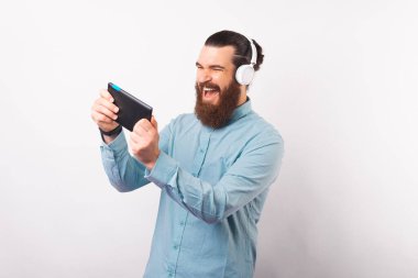 Neşeli, gülümseyen sakallı adam beyaz arka planda video oyunları oynuyor.