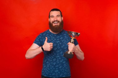 Sakallı yakışıklı adam mutlu ve pozitif gülümsüyor, başparmağı mükemmel ve onay işareti yapıyor.