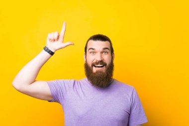Neşeli genç sakallı adam bir stüdyoda sarı arkaplanı işaret ediyor..