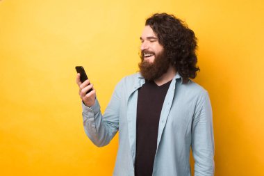 Sakallı adam cep telefonu kullanır, mesajlara cevap verir sarı arkaplanda arkadaşınla çevrimiçi sohbet eder.