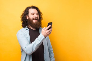 Sakallı adamın cep telefonu kullanırken, arkadaşlarına mesaj yazarken, sarı arka planda.