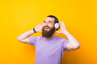 Mutlu sakallı bir adamın gülümsemesi kulaklıkla müzik dinliyor, sarı duvarlı arka plan