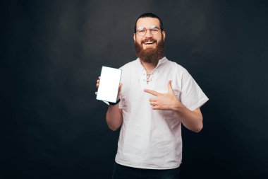 Gülümseyen sakallı adam tabletini siyah arka planda gösteriyor..