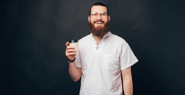 Gülümseyen sakallı adam elinde siyah arka planda bir fincan tutuyor..