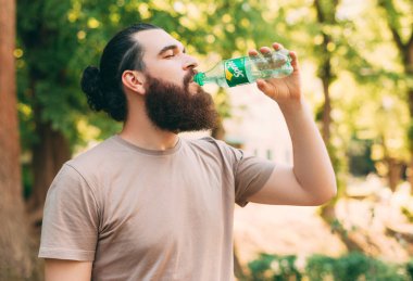 CHISINAU, MOLDOVA, 9, Haziran 2021: Genç sakallı adam açık havada sprite içiyor.