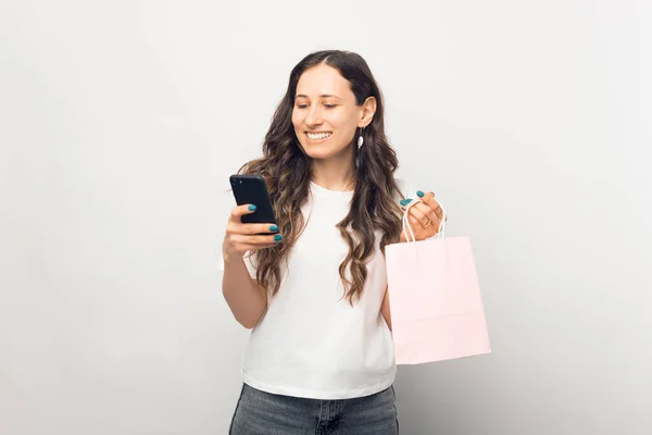Menina bonita está segurando um saco de compras, enquanto encomendar algo ou pagar por telefone. — Fotografia de Stock