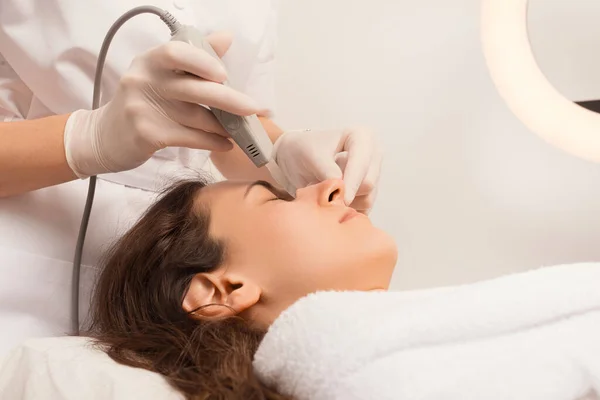 Cosmetoloog is het schoonmaken van een vrouw gezicht met de echografie spatel. — Stockfoto