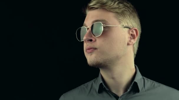 Portrait de jeune homme en lunettes de soleil sur fond sombre — Video