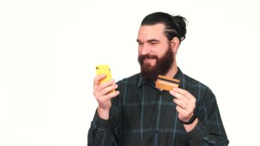 Akıllı telefon ve kredi kartı kullanan gülümseyen sakallı adamın görüntüsü.