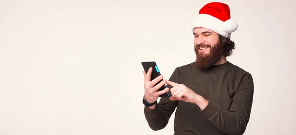 タブレットを使用しているクリスマスの帽子をかぶっている髭の男のバナーサイズの写真. — ストック写真