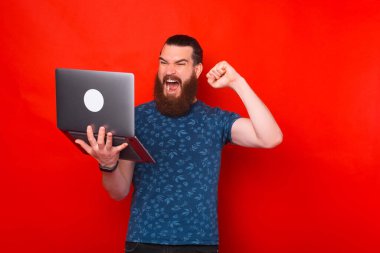 Heyecanlı sakallı adam elinde tuttuğu dizüstü bilgisayara bakarken kazanan hareketi yapıyor ve çığlık atıyor..