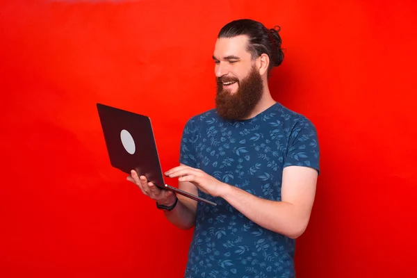 Smiling bearded man is holding his laptop is typing or surfing. — Stock Photo, Image