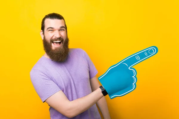 Hombre barbudo excitado está señalando a un lado con el guante del ventilador de espuma que está usando. — Foto de Stock