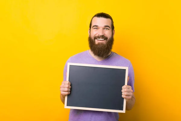 Lächelnder Mann hält eine kleine Tafel über gelbem Hintergrund. — Stockfoto