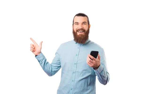 Hombre alegre está apuntando sobre el fondo blanco mientras sostiene su teléfono. — Foto de Stock