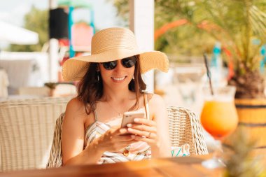 Genç bir kadın kokteyl içerken cep telefonuyla yazı yazıyor..