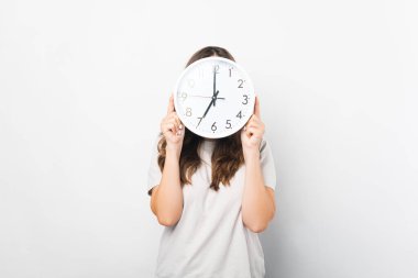 Beyazlar içindeki kadın, yuvarlak bir saatle yüzünü tutuyor ve örtüyor..