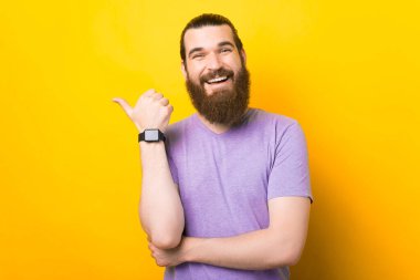 Sakallı adam sarı arka planda baş parmağını gösteriyor..