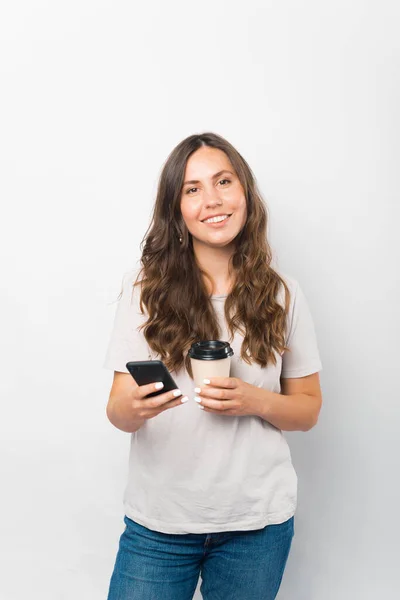 Foto verticale di una giovane donna che tiene il telefono e una tazza di caffè da portare via. — Foto Stock