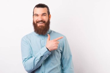 Gülümseyen sakallı adam beyaz arka planı işaret ediyor..