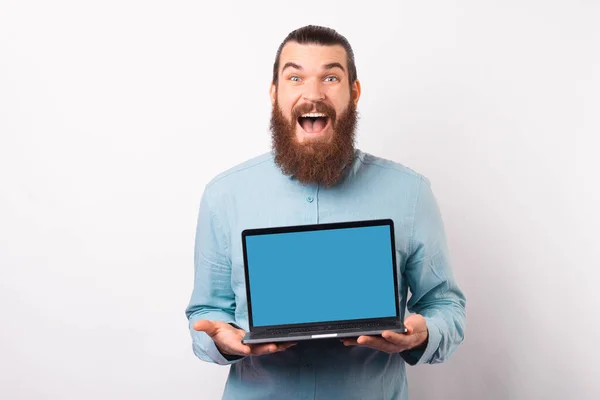 Emocionado hombre barbudo está mostrando a la cámara la pantalla de su portátil. — Foto de Stock