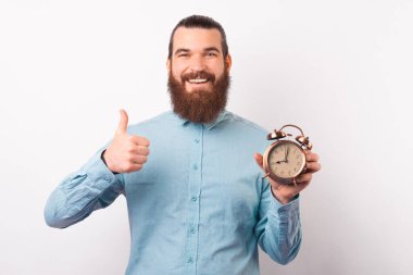 Erkek işadamı elinde çalar saat tutuyor ve kameraya başparmağını gösteriyor..