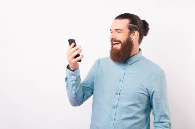 Mutlu sakallı adam telefonunu ve kulaklıklarını kullanıyor..