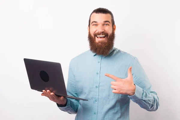 Sonriendo a la cámara hombre barbudo está apuntando a la computadora portátil que está sosteniendo. — Foto de Stock