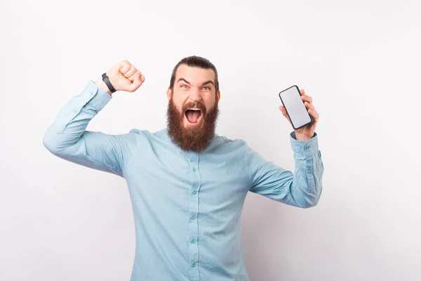 Bärtiger Mann feiert Sieg, während er sein Handy in der Hand hält. — Stockfoto