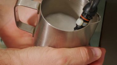 Bir el zarif bir şekilde parlak bir metal sürahiyi tutarken buhar yavaşça sütü köpürüyor ve güzel bir kahve sanatı yaratıyor.