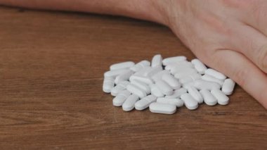 Uyuşturucuya hayır de. Beyaz hapların bir koleksiyonu ahşap bir yüzeye düzgünce yığılırken bir el onlarla etkileşime giriyor..