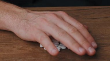 Bir el, düzgün ilaç kullanımının önemini vurgulayarak, tahta bir masanın üzerindeki beyaz hapların üzerine uzanır.