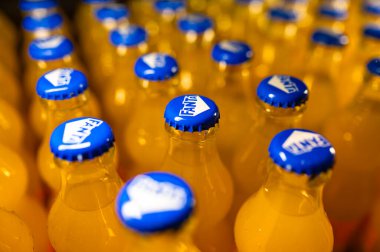 Chisinau, Moldova, 2 Aralık 2025. Mavi kapaklar, parlak ambalajlar ve tekrarlanan şablonlar gösteren turuncu soda şişelerinin yakın çekim sıraları.