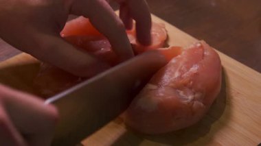 Çiğ tavuk kesim tahtasında dilimleniyor, eller şef bıçaklarına üniforma parçaları için rehberlik ediyor, proteini kızartma için hazırlıyor.