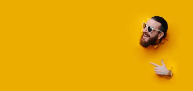 Sarı arka plandan çıkan adam kafası, güneş gözlüğü ve kalın sakal takıyor, işaret eden parmak tabancası jesti...,