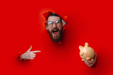 Sakallı Adam Domuz Kumbarası ve Gösterişli İfade ve Dramatik Aydınlatma Tutarken Kırmızı Kağıt Kırıyor,