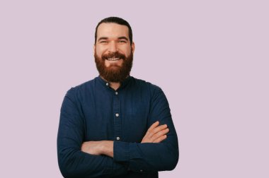 Sakallı, sırıtan beyaz adam çapraz kollar, donanma gömleği, yumuşak pembe arka plan, arkadaş canlısı özgüvenli ifade.,