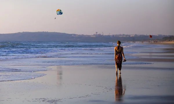 Genç bir kadın boş bir kumsalda gökyüzünden düşen göksel ışık huzmelerine doğru yürüyor.