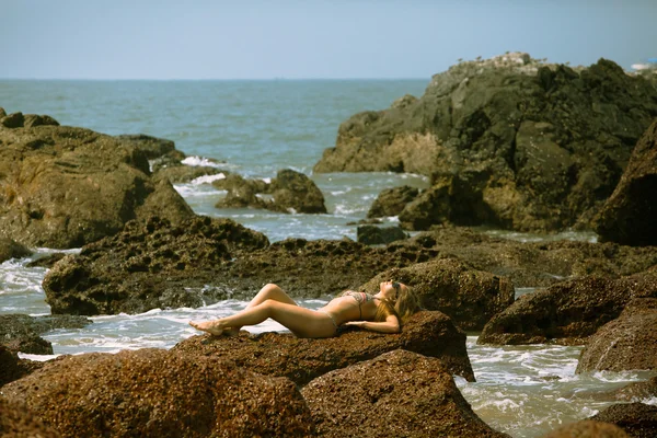Молодая девушка в бикини с красивым телом и солнцезащитными очками возле красных камней на пляже — стоковое фото