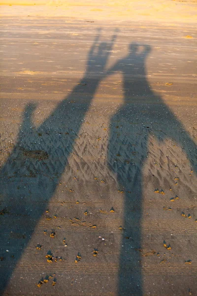 The shadow of two embracing lovers on the yellow sand of the beach.