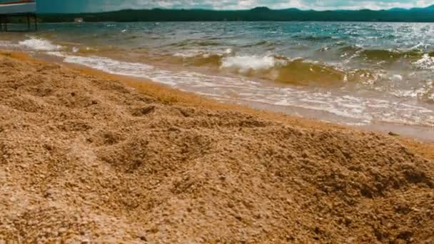 Vågorna kraschar försiktigt på lugnt sandstrand. Mountain bakgrund. 4 k film — Stockvideo