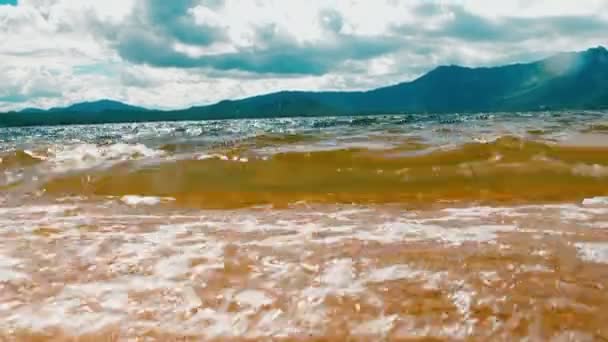 Ondas batendo suavemente na praia de areia tranquila. fundo da montanha. Filmagem 4K — Vídeo de Stock