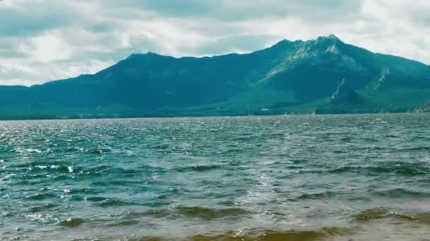 Las olas se estrellan suavemente en la tranquila playa de arena. fondo de montaña. Imágenes 4K — Vídeo de stock