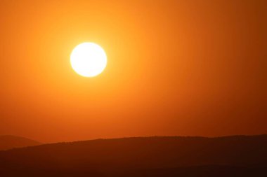Siluetli tepelerin üzerinde gün batımı parlak turuncu ışık ve parlayan güneşle